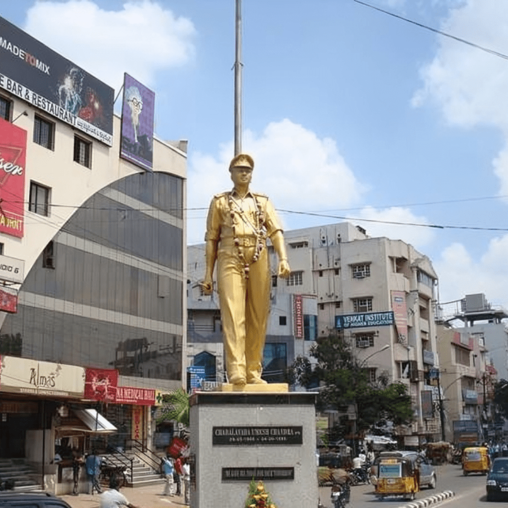 Statue of police officer Umesh Chandra in SR Nagar, Hyderabad, surrounded by local businesses and Website traffic.